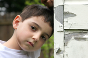 Image of sad little boy leaning against a building